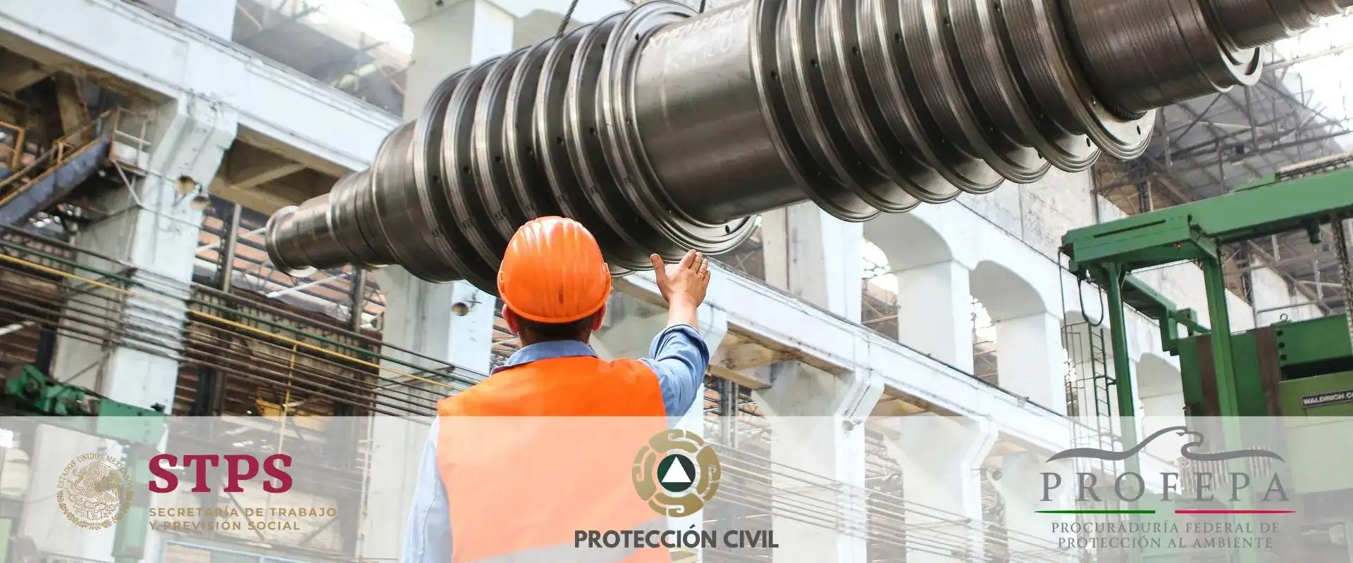 Persona con chaleco y casco naranja dando indicaciones a una grúa en área industrial